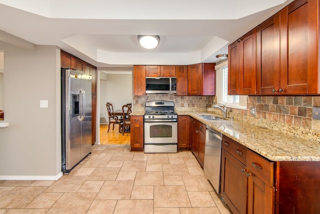 kitchen with stainless steel appliances, backsplash, a sink, light stone countertops, and baseboards