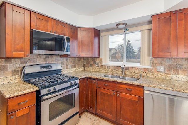 kitchen featuring stainless steel appliances, a sink, backsplash, and light stone countertops