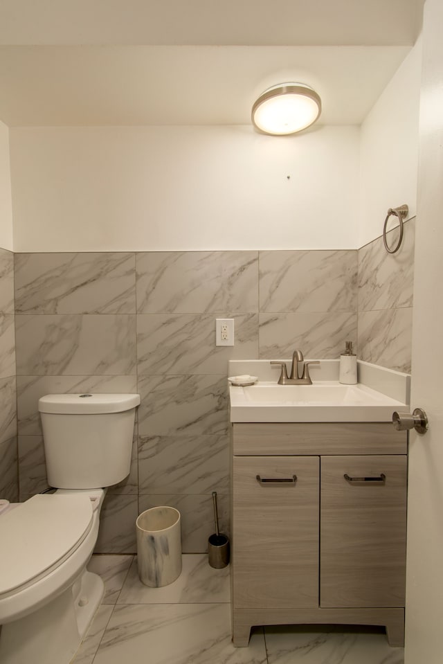 half bath with toilet, marble finish floor, and vanity