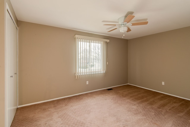 carpeted empty room featuring a ceiling fan, visible vents, and baseboards