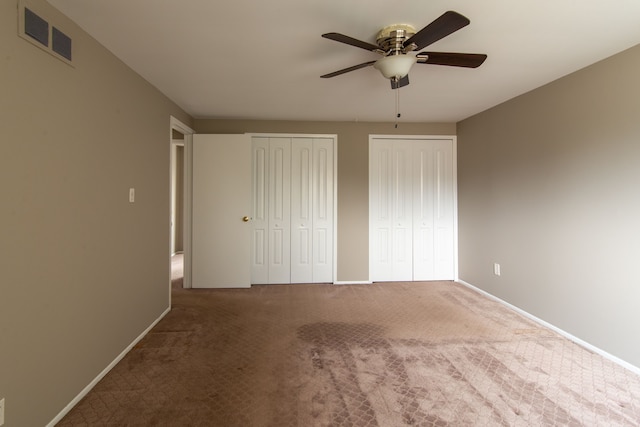 unfurnished bedroom with ceiling fan, visible vents, baseboards, multiple closets, and carpet