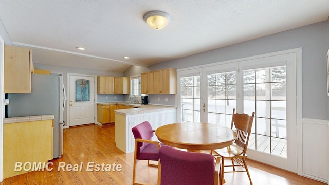 kitchen featuring tile counters, light wood-style flooring, a peninsula, vaulted ceiling, and a sink