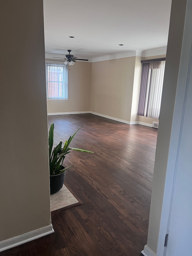 spare room with dark wood-type flooring, a ceiling fan, visible vents, and baseboards