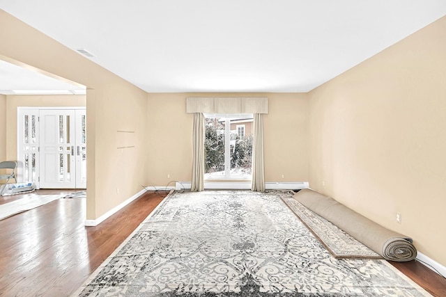 unfurnished room featuring a baseboard radiator, visible vents, baseboards, and wood finished floors