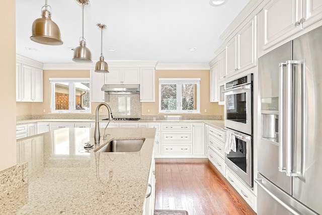 kitchen featuring white cabinets, decorative light fixtures, stainless steel appliances, under cabinet range hood, and a sink