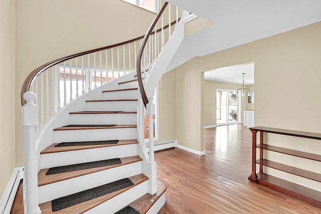 stairs featuring a notable chandelier, a baseboard radiator, wood finished floors, and baseboards