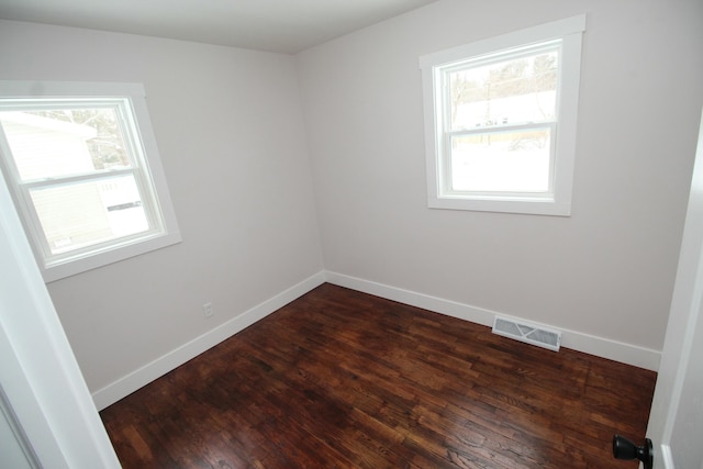 spare room featuring dark wood finished floors, visible vents, and baseboards