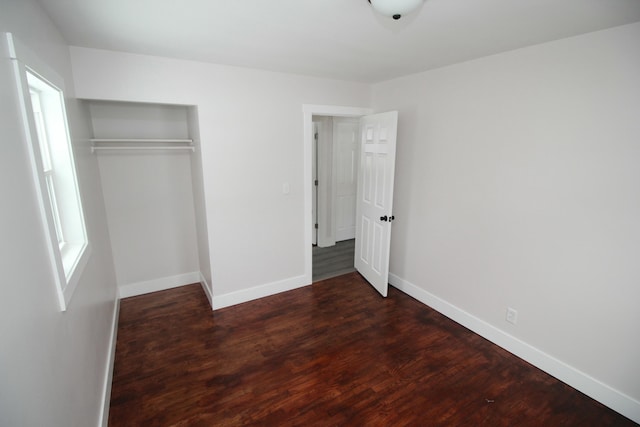 unfurnished bedroom with a closet, dark wood finished floors, and baseboards