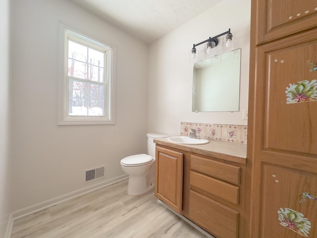 bathroom with visible vents, toilet, vanity, wood finished floors, and baseboards