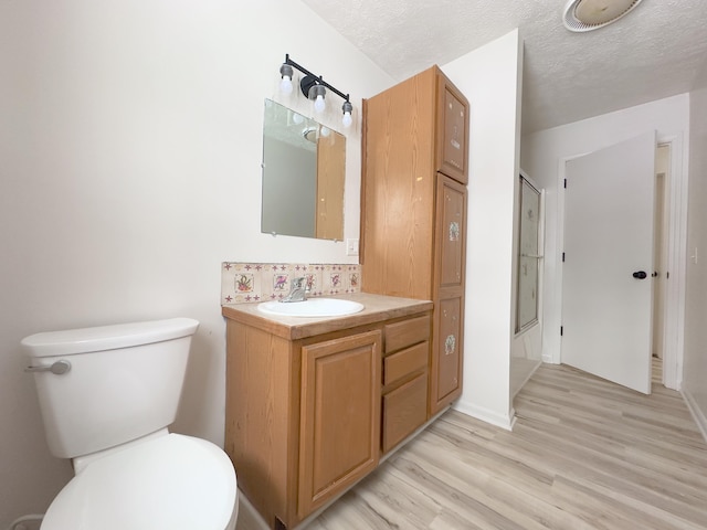 full bath with toilet, wood finished floors, combined bath / shower with glass door, a textured ceiling, and vanity