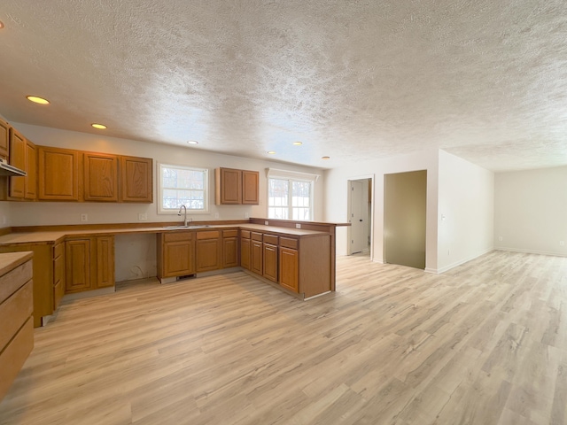 kitchen featuring a peninsula, light wood-style flooring, brown cabinets, and a sink