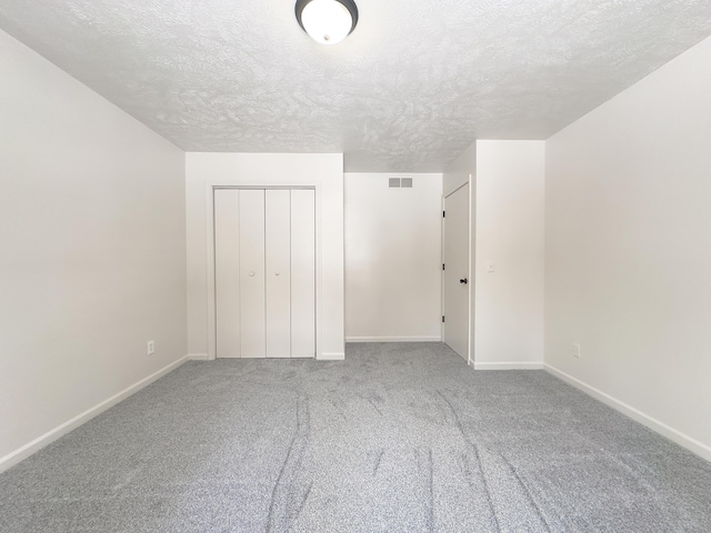 unfurnished bedroom featuring a textured ceiling, carpet flooring, visible vents, baseboards, and a closet