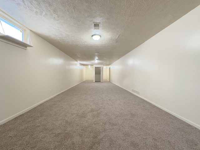 below grade area featuring baseboards, a textured ceiling, visible vents, and carpet flooring