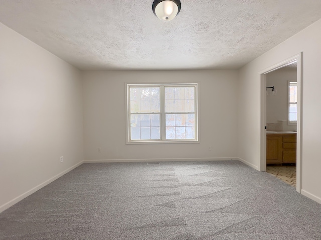 empty room featuring light carpet, baseboards, and a textured ceiling