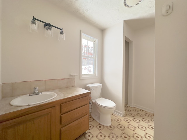 half bath with visible vents, toilet, vanity, a textured ceiling, and baseboards