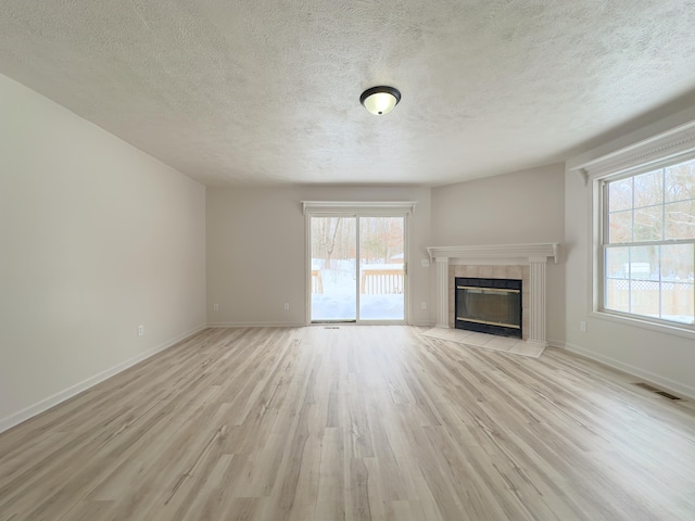 unfurnished living room with visible vents, a tiled fireplace, light wood-style floors, a textured ceiling, and baseboards