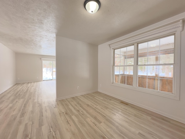 empty room featuring light wood-style flooring, visible vents, baseboards, and a textured ceiling