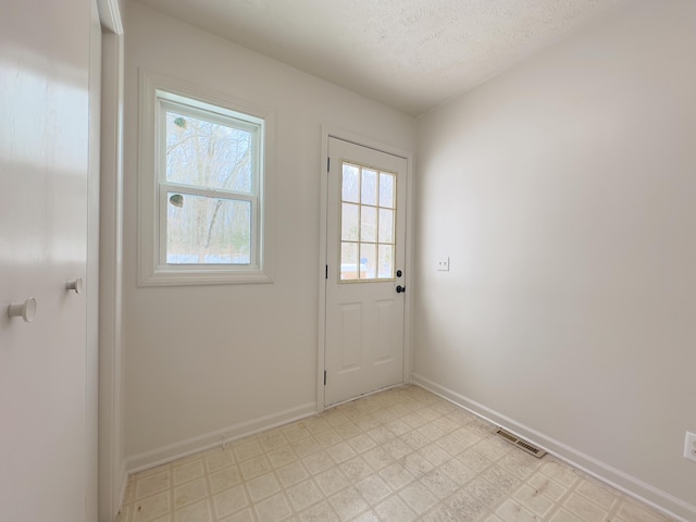 doorway featuring a textured ceiling, light floors, visible vents, and baseboards