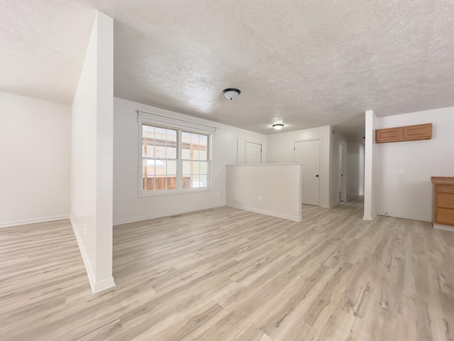 unfurnished living room with light wood-style floors, a textured ceiling, and baseboards