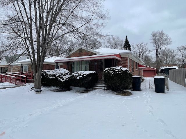 snow covered property featuring a garage, brick siding, and fence