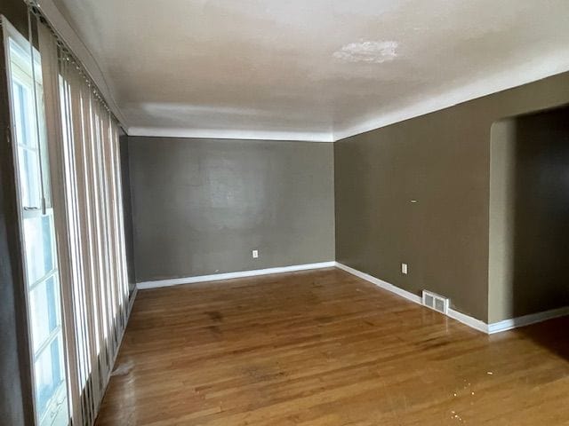 empty room with wood finished floors, visible vents, and baseboards