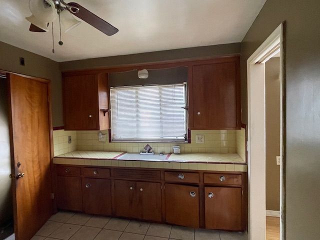 kitchen with tile countertops, ceiling fan, light tile patterned flooring, a sink, and decorative backsplash