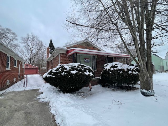 view of snow covered exterior with a garage, brick siding, and a chimney