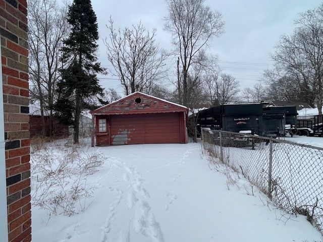 snowy yard with an outbuilding, fence, and a detached garage