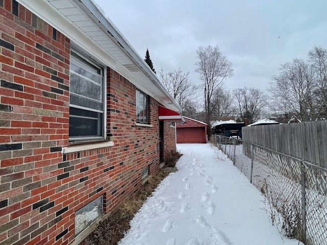 snow covered property featuring a garage, fence, and brick siding