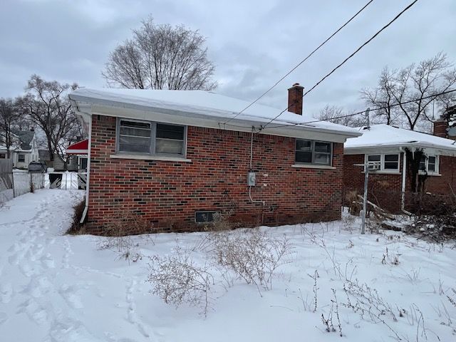 view of snowy exterior with a chimney and brick siding