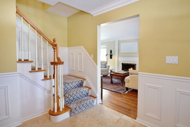 staircase featuring a warm lit fireplace, crown molding, baseboards, and tile patterned floors