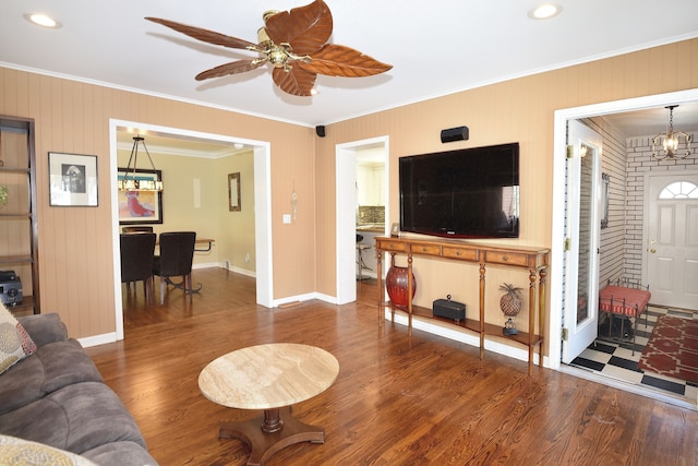 living area featuring ceiling fan with notable chandelier, ornamental molding, dark wood-style flooring, and baseboards