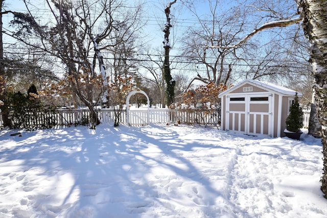 yard layered in snow featuring a storage shed, a detached garage, fence, and an outdoor structure