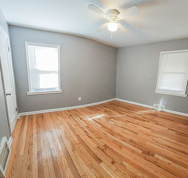 empty room with light wood finished floors, a ceiling fan, visible vents, and baseboards