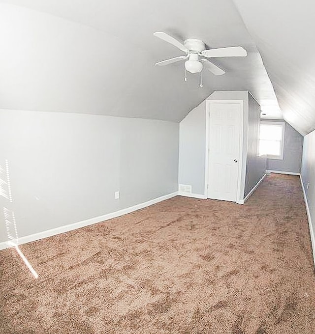 bonus room with lofted ceiling, dark carpet, a ceiling fan, and baseboards