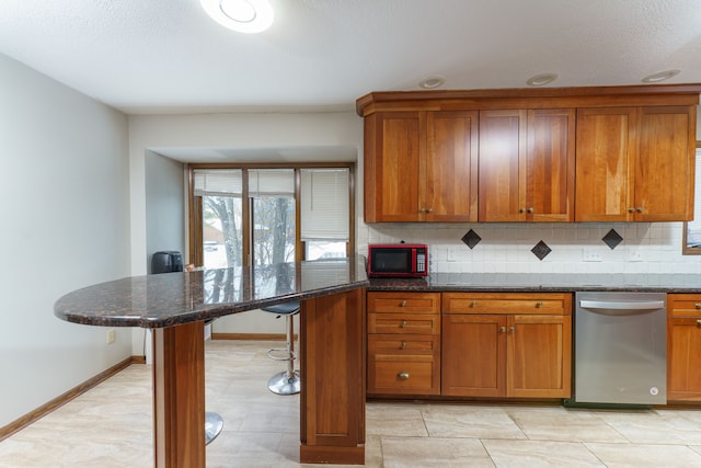 kitchen with a breakfast bar, tasteful backsplash, brown cabinetry, dark stone countertops, and dishwasher