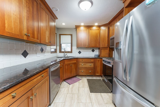 kitchen featuring stainless steel appliances, dark stone counters, brown cabinetry, and a sink