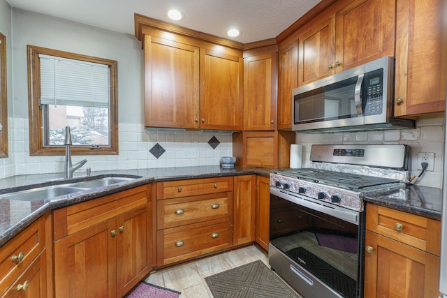 kitchen featuring appliances with stainless steel finishes, dark stone counters, brown cabinets, and a sink