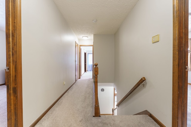 corridor with light colored carpet, a textured ceiling, and an upstairs landing