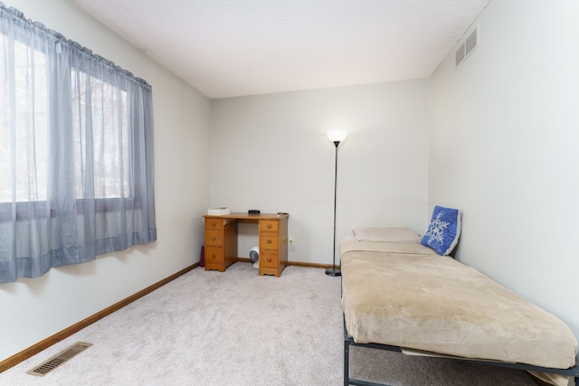 bedroom featuring light colored carpet, visible vents, a textured ceiling, and baseboards