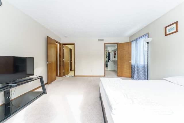 bedroom featuring light colored carpet, visible vents, baseboards, a closet, and a walk in closet