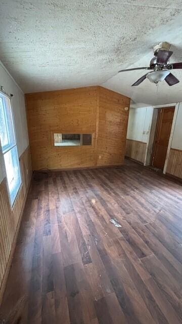 additional living space featuring ceiling fan, a textured ceiling, lofted ceiling, wooden walls, and dark wood-style floors