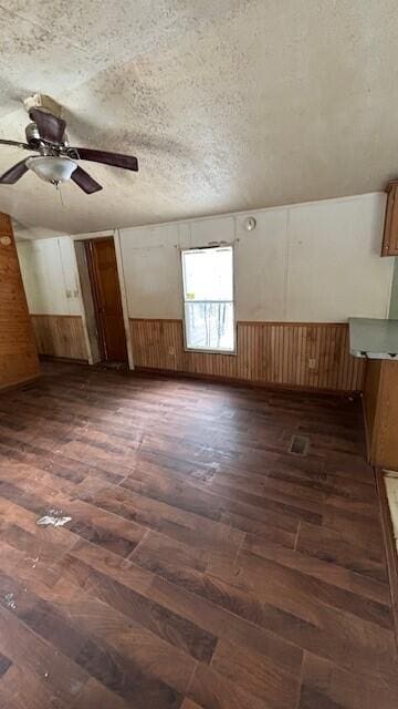 additional living space with a textured ceiling, wood walls, dark wood-style flooring, and a wainscoted wall