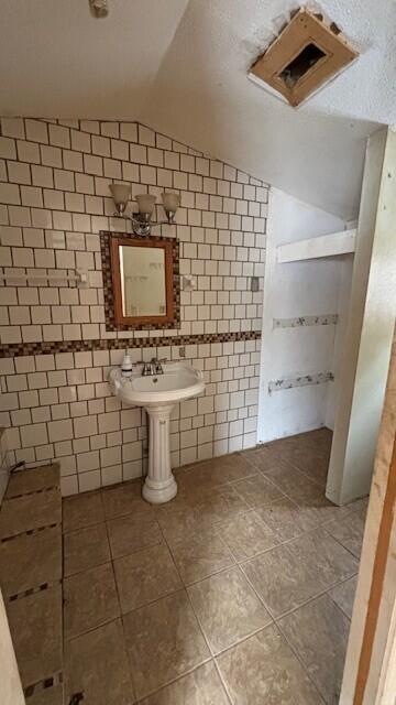 bathroom with tile patterned flooring, vaulted ceiling, and tile walls