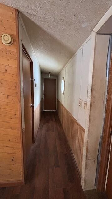 hallway with a wainscoted wall, wooden walls, dark wood-style flooring, and a textured ceiling