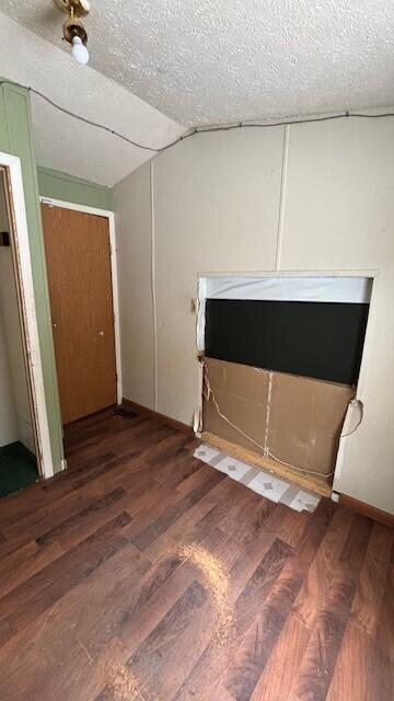 unfurnished bedroom featuring a textured ceiling, vaulted ceiling, and dark wood-type flooring