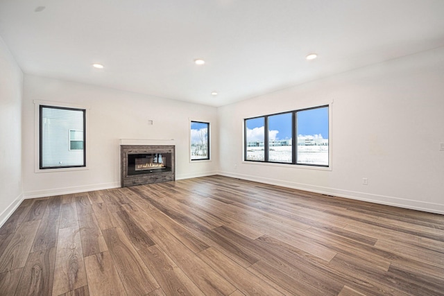 unfurnished living room with a glass covered fireplace, recessed lighting, wood finished floors, and baseboards