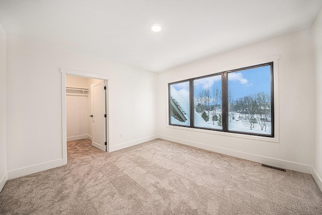 unfurnished bedroom featuring a closet, light colored carpet, visible vents, a spacious closet, and baseboards