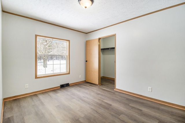 unfurnished bedroom with visible vents, ornamental molding, a textured ceiling, wood finished floors, and baseboards