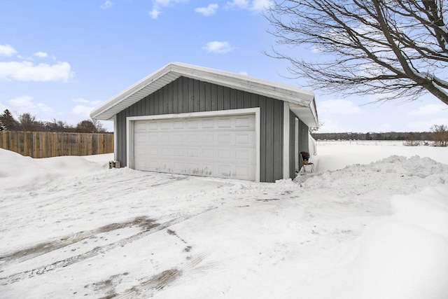 snow covered garage with a detached garage and fence